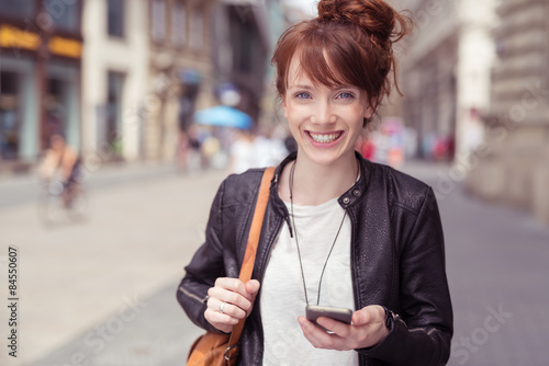 glückliche junge frau geht mit den handy durch die innenstadt photo