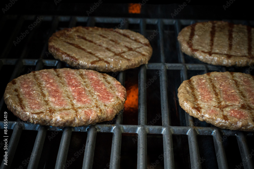 Four beef hamburger slices on grill rack, soft focus
