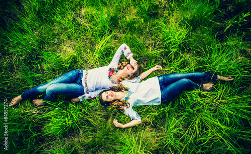 Two happy pretty girls lying on the green grass