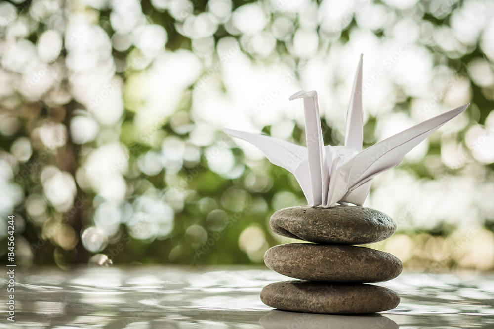 Obraz premium Origami crane, paper bird and zen stones on bokeh background. sh