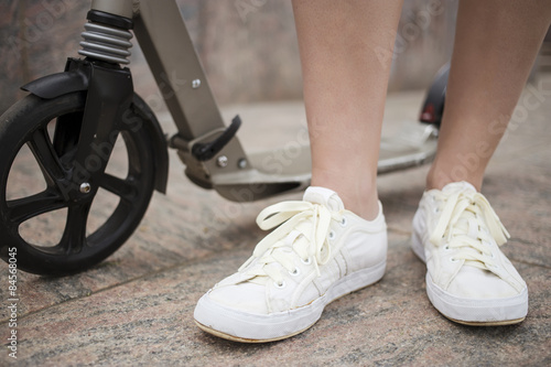 Scooter and feet of a man who stands on the granite pavement