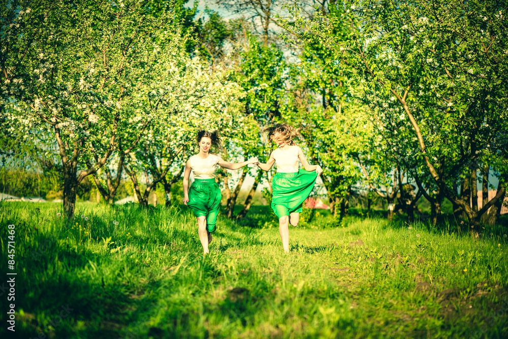 Two happy pretty girls walking on the apple trees garden Two happy pretty girls walking on the apple trees garden
