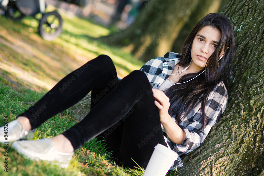 Young woman relaxing in Central Park with a coffee cup while lis Young woman relaxing in Central Park with a coffee cup while lis
