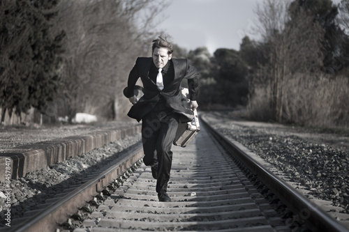 hombre con traje y maleta antiguos corre por las vías del tren