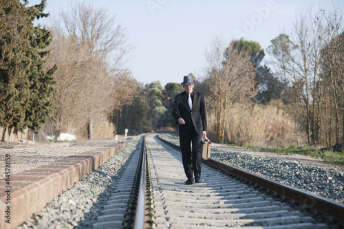 Hombre con traje y maleta antiguos camina por raíles de tren