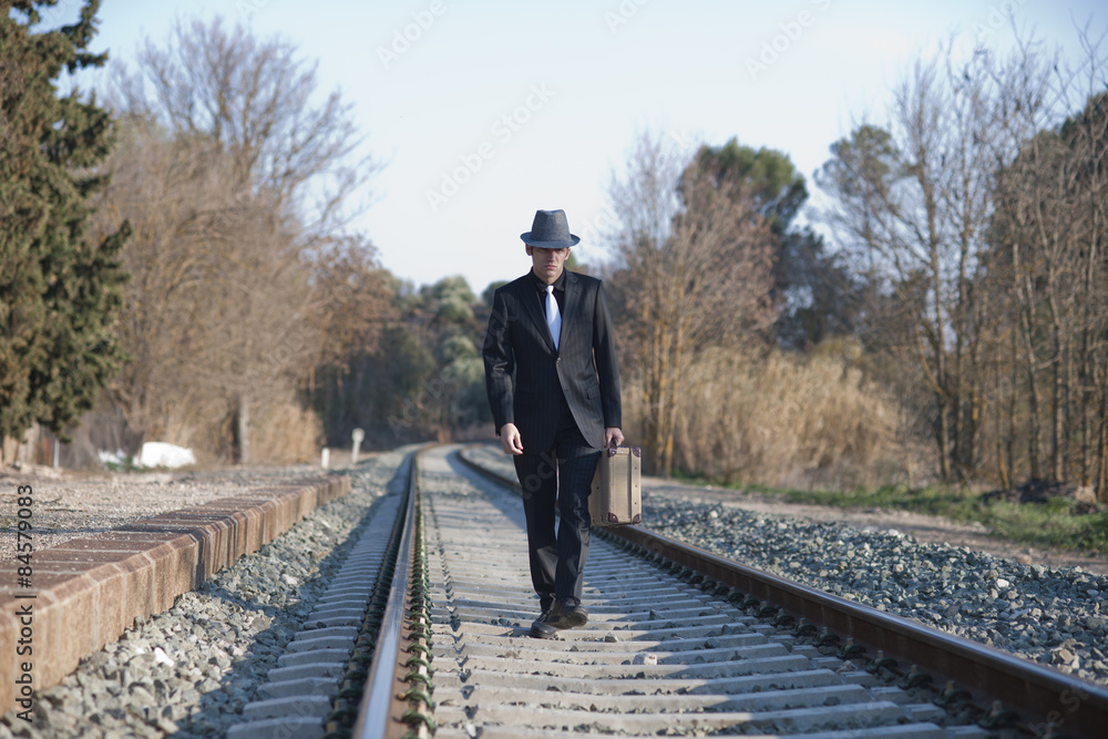 Hombre con traje y maleta antiguos camina por raíles de tren