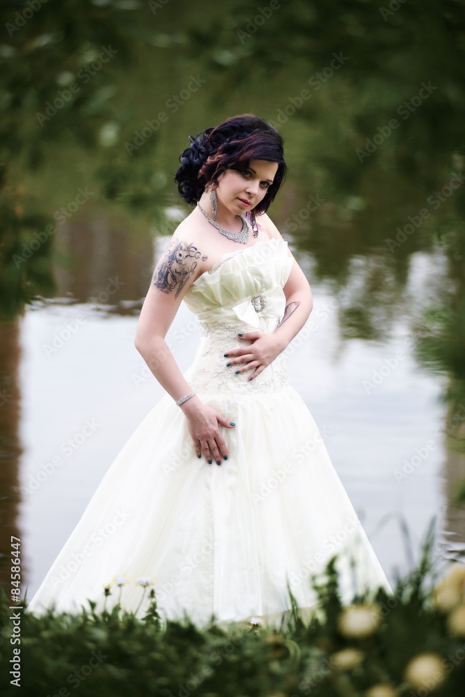 Beautiful young bride in white dress near lake in summer green park