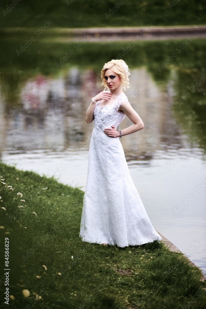 Beautiful young bride in white dress near lake in summer green park Beautiful young bride in white dress near lake in summer green park
