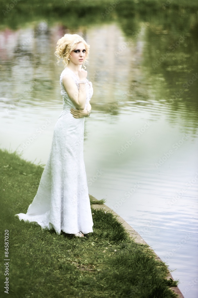 Beautiful young bride in white dress near lake in summer green park Beautiful young bride in white dress near lake in summer green park