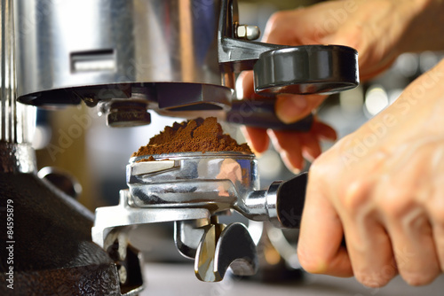 Barista dispensing ground coffee from a grinder into a portafilter