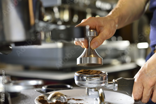 Barista using a tamper to press ground coffee into a portafilter