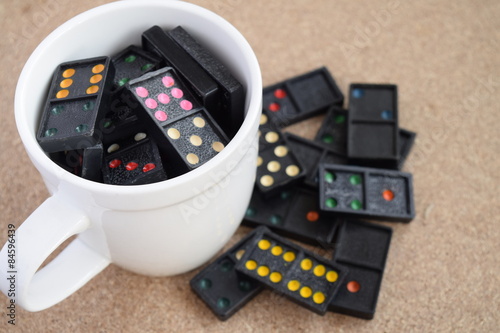 Black Dominoes in coffee cup on wooden background