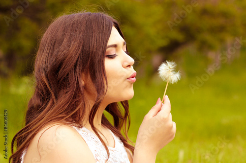 beautiful young girl sitting on the grass and blowing on a dandelion. warm summer day photo