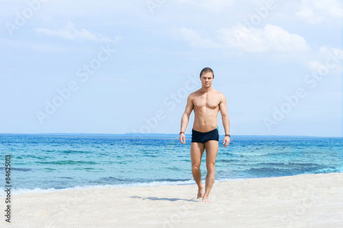 Young  fit and handsome man with athletic and muscled body walking on a summer beach