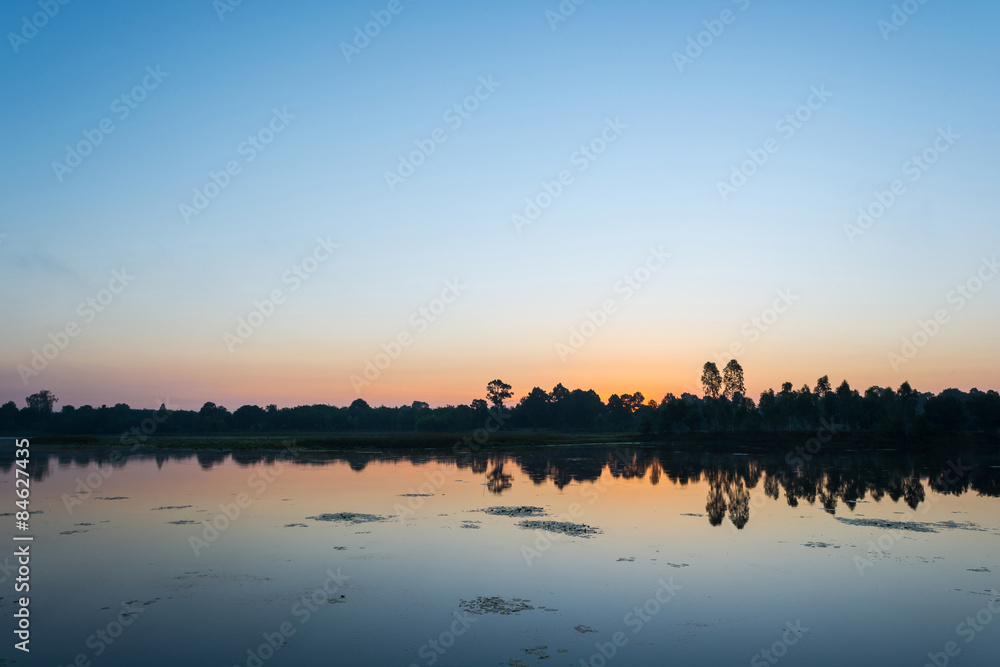 Beautiful sunrise over calm lake. Colorful and vibrant landscape of lake shore. Tranquil landscape useful as background
