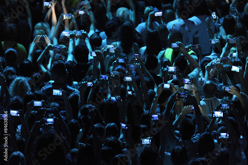 Excited youngsters attending a show, applauding and taking videos vith cell phones