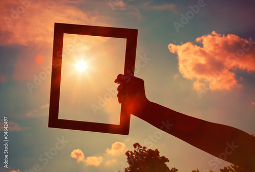 Hand holding a wooden frame on sunrise sky background. Care, saf