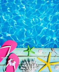 flip-flop, starfish, seashells and coral on wooden plank and pool - summer background
