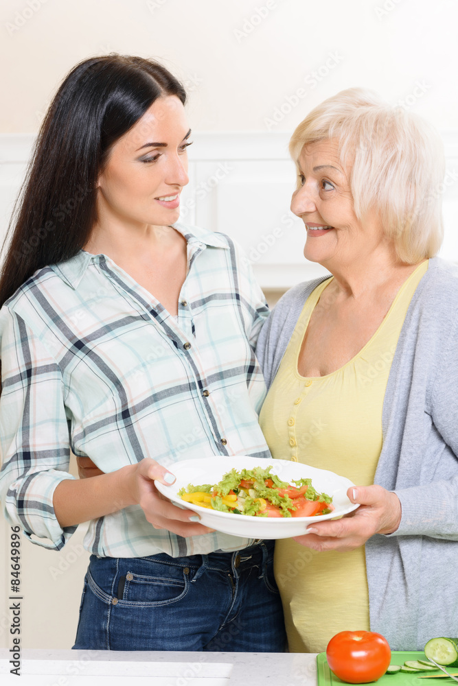 Pair of women holding salad in kitchen
