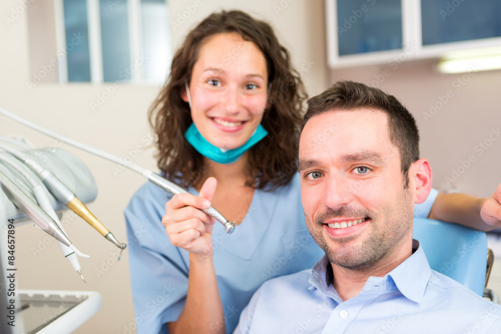 Portrait of a young attractive dentist in his office with patien Portrait of a young attractive dentist in his office with patien