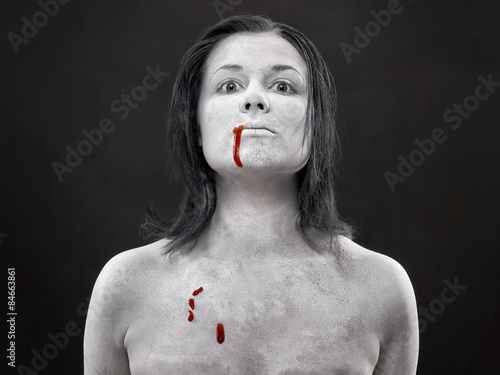 Zakrwawiona kobieta pomalowana na biało na ciemnym tle