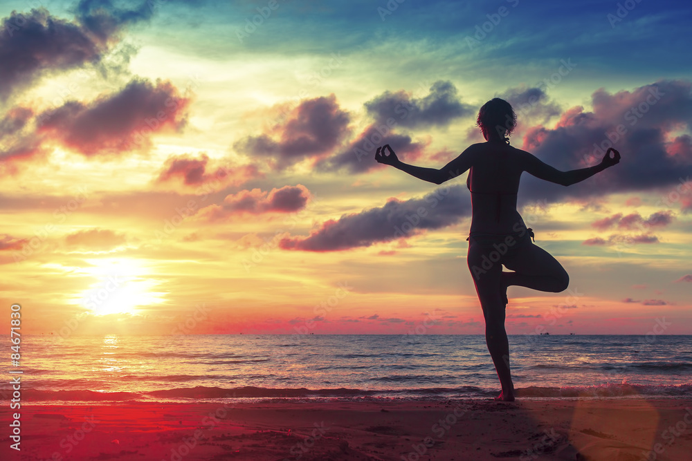 Silhouette  woman practicing yoga on the beach at surrealistic sunset. 