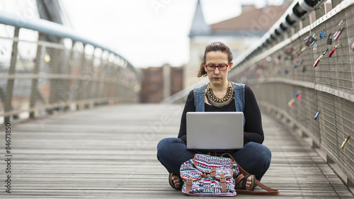 Young woman working on laptop while sitting on the street. Blogger.