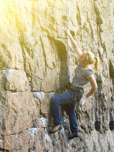 Young woman with rope climbs on the rock.