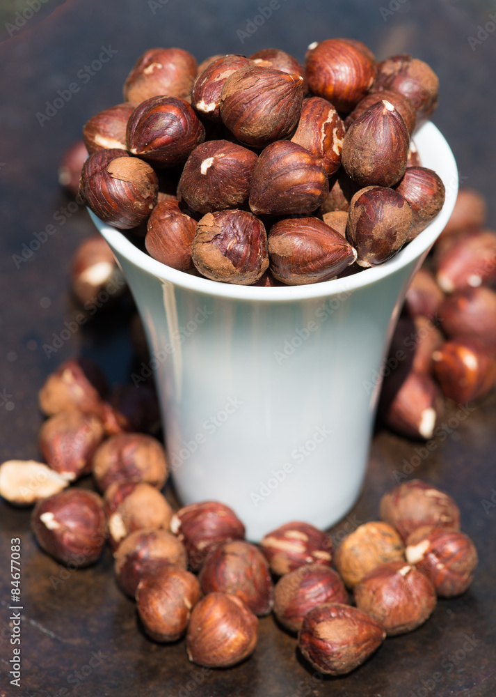 Fototapeta premium Raw hazelnuts, no shell, in a white cup on rustic brown background.