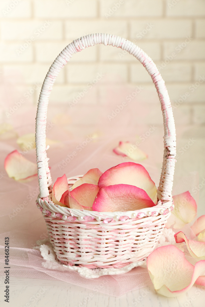 Wedding basket with roses petals on table, on light background