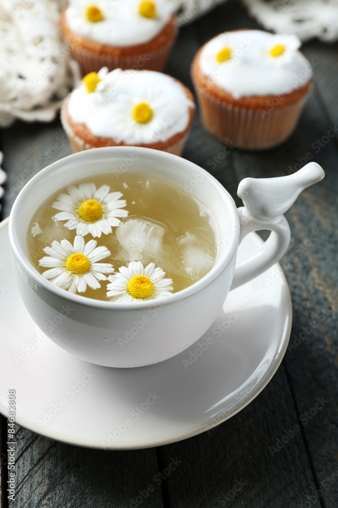Cup of chamomile tea with chamomile flowers and tasty muffins on color wooden background Cup of chamomile tea with chamomile flowers and tasty muffins on color wooden background