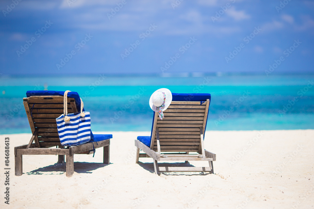 White hat and bag on lounge chairs at tropical sandy beach 