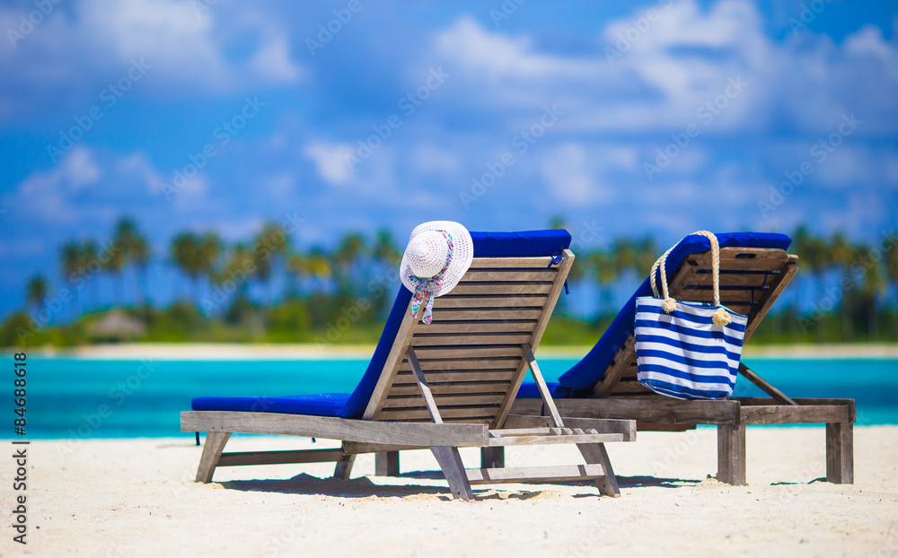 White hat and bag on lounge chairs at tropical sandy beach 