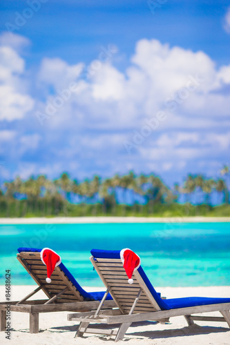 Two loungers with red Santa hats on tropical beach with white