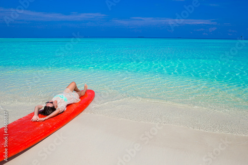 Young surfer woman at white beach on red surfboard
