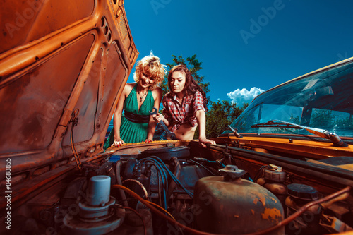 Beautiful woman mechanic is repairing a car another woman is watc