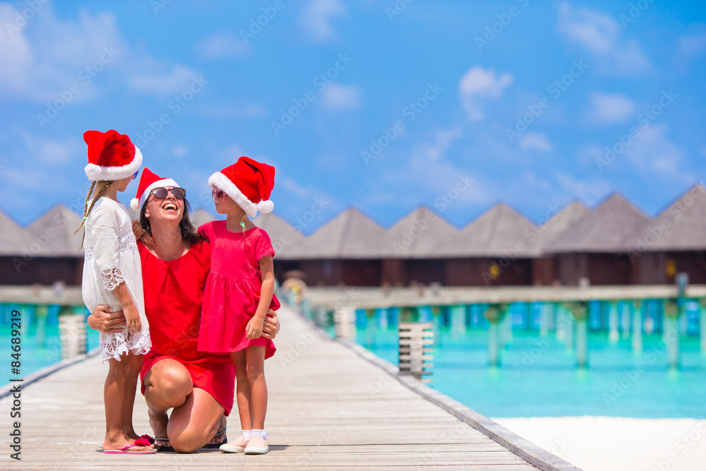 Obraz premium Happy mother and little girls in Santa hat near water villa on