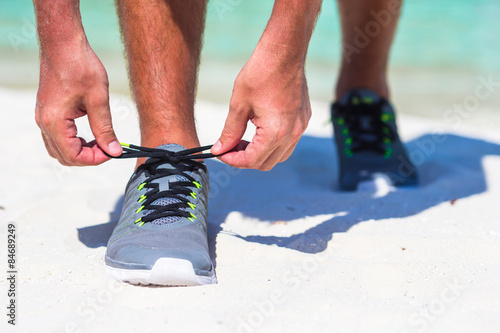 Running man tying running shoe laces on white beach