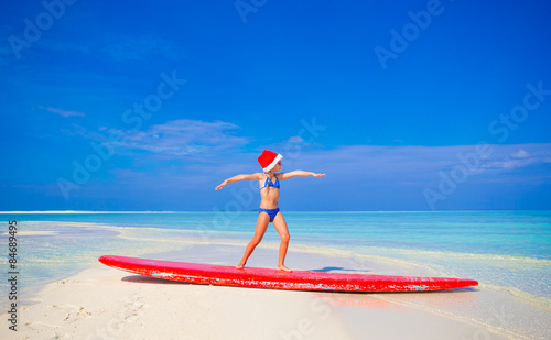 Adorable little girl in Santa hat practice surfing position on