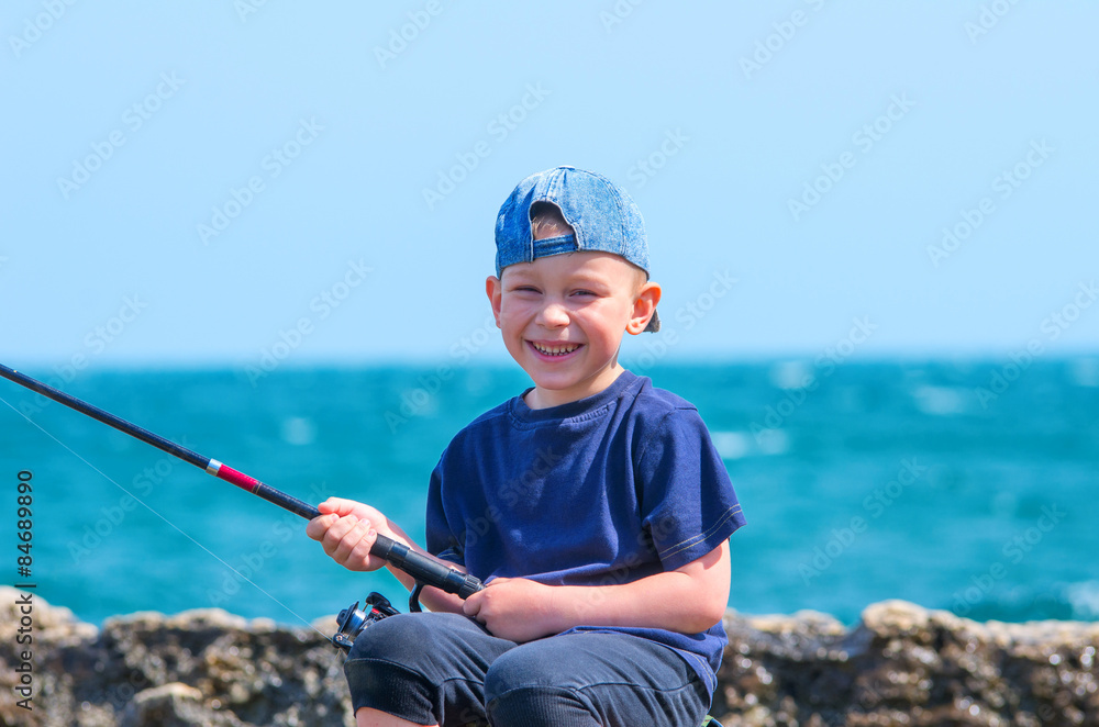 Little boy on sea fishing, holding a fishing rod and smiles Little boy on sea fishing, holding a fishing rod and smiles
