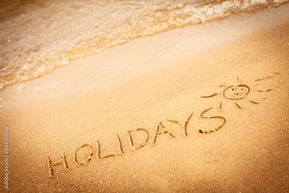 Fototapeta premium The word holidays written in the sand on a beach