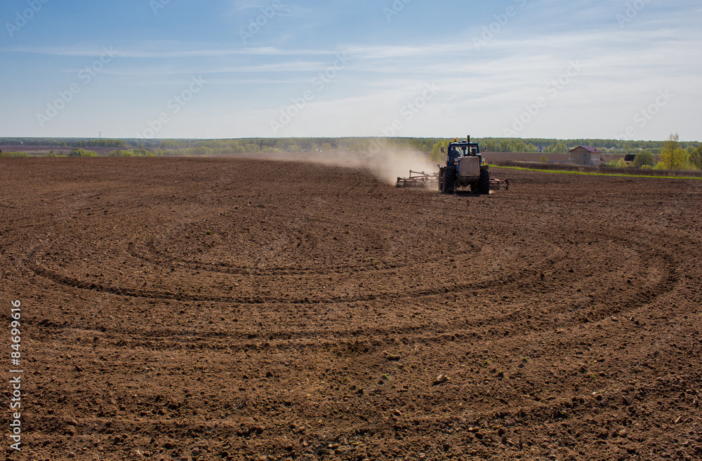 Fototapeta premium Blue tractor plowing a field before planting