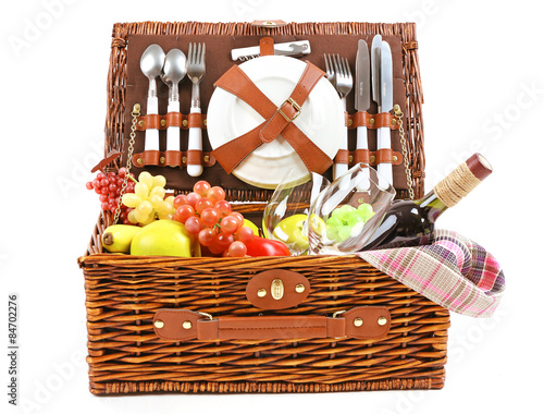 Wicker picnic basket with food, tableware and tablecloth isolated on white