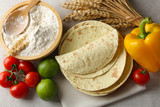 Stack of homemade whole wheat flour tortilla and vegetables on light background