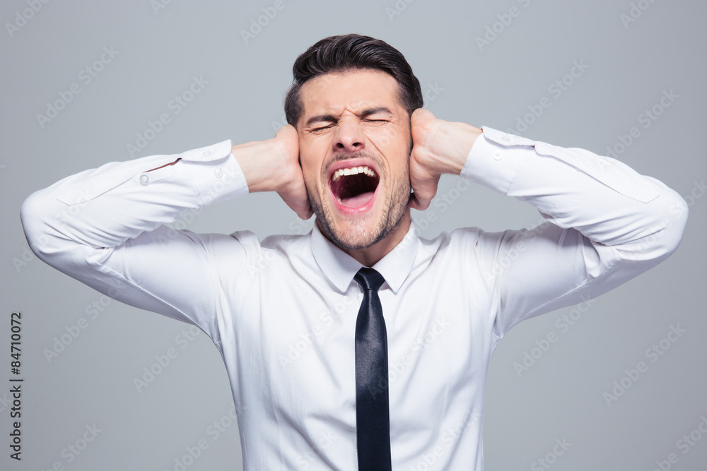 Businessman covering his ears and screaming Businessman covering his ears and screaming