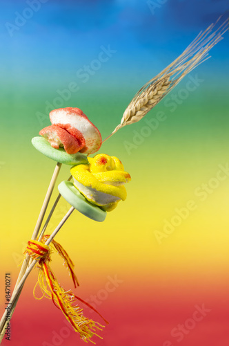 Red and yellow sugar candy roses and one ear of wheat, in rainbow satured background (blue, green, yellow, red) photo