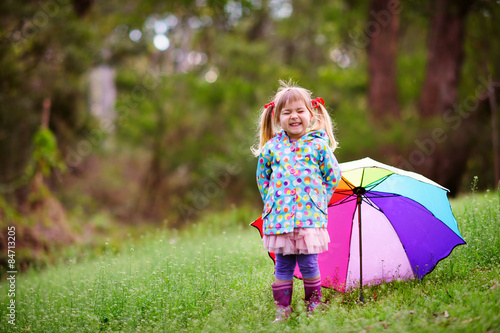 Happy little girl with umbrella in raincoat at green grass backg