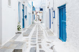 Mykonos, Greece - Traditional whitewashed street of Mykonos town with blue windows and doors on a sunny summer morning. Empty alleyway at sunrise