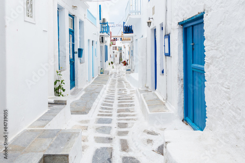 Mykonos, Greece - Traditional whitewashed street of Mykonos town with blue windows and doors on a sunny summer morning. Empty alleyway at sunrise