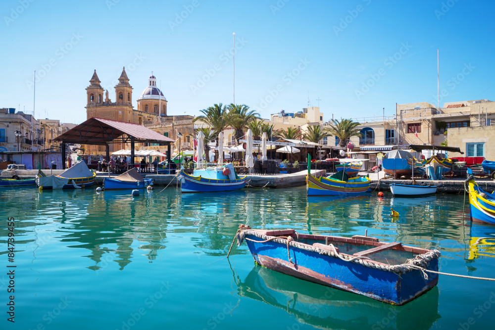 Marsaxlokk, Malta - Traditional Luzzu fishing boats at Marsaxlokk market with clear blue sky and turquoise sea water on a sunny summer day
